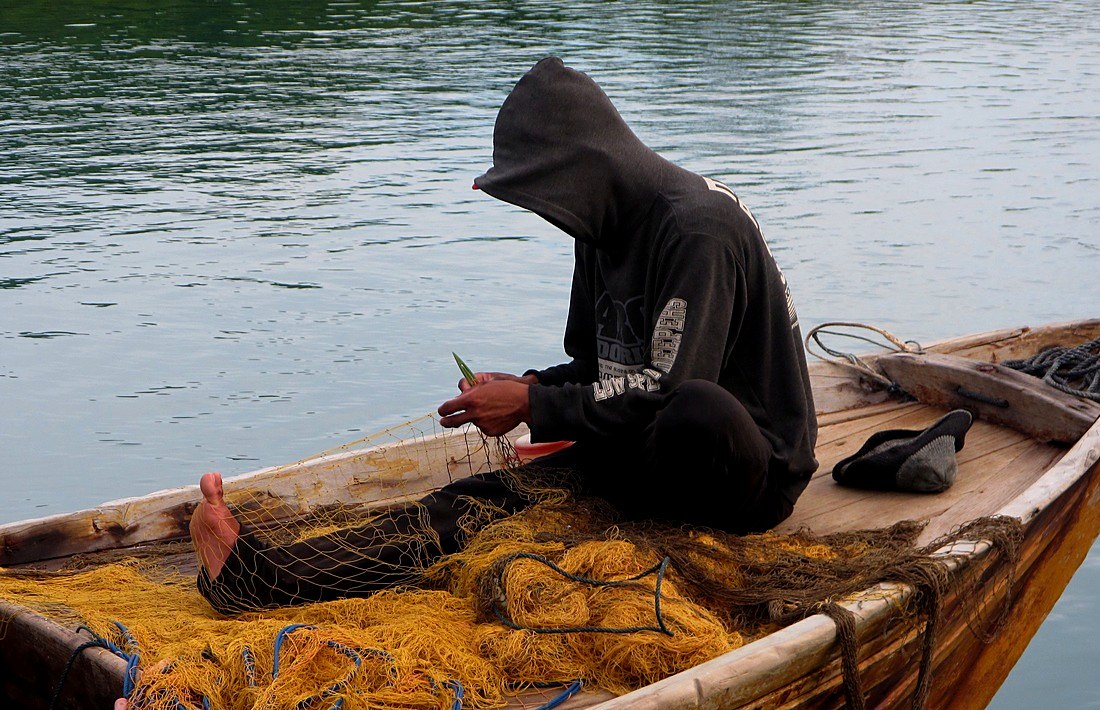Fisherman mending nets in the hired boat, Merapas